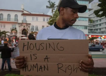 A group of protesters calling for better treatment of Miami-Dade County’s homeless population shouted over the din coming from thumping bars and restaurants on Ocean Drive around 7 p.m. Saturday. “Rent is rising all the time. Homelessness is not a crime!” the group chanted as Drake and Rihanna songs played from South Beach bars across the street. The Miami Coalition to Advance Racial Equity held a “sleepover” protest in Lummus Park on Saturday night in solidarity with Miami-Dade’s homeless population. Their plan is to spend the night in the park, even as the outer bands of Tropical Storm Debby sent gusty winds and squalls over South Florida. Citing Miami Beach’s expected crackdown on unsheltered homeless people outdoors this month, David Peery, the executive director of the coalition, said he expects police to arrest protesters after the park closes at 10 p.m. At a news conference earlier this week, Miami Beach Mayor Steven Meiner said police would be enforcing the city’s anti-camping ordinance that prohibits sleeping in public. Violating the ordinance can result in a $500 fine and up to 60 days in jail. Read more: Miami Beach to crack down on homeless residents sleeping outside in August Saturday night brought strong winds to Miami Beach. Lightning was popping in the sky within the first hour of the protest, and it started raining heavily around 9 p.m. Jonathan Gartrelle, a Miami Beach activist, led protesters in chants as they displayed a banner to passersby on Ocean Avenue. Some walking by took up the chants, echoing that homeless people want “housekeys, not handcuffs.” Protesters hold up a sign during a protest at Lummus Park in Miami Beach on Saturday August 3rd, 2024. Alexia Fodere for The Miami Herald Others piped up to oppose the group’s message. “Close the border!” shouted one man driving past on a golf cart. Addressing the more than a dozen people gathered to protest on Saturday evening, Peery called for an end to the “cruel” and “inhumane” treatment of homeless people in Miami Beach and throughout Miami-Dade County. “We want [people] to know that what Miami Beach is doing is outrageous,” Peery said. Peery and his organization say Miami Beach’s anti-camping ordinance criminalizes homelessness. Instead of jailing people for sleeping outside, Peery said he supports a housing-first approach that would provide unconditional, permanent housing to people experiencing homelessness. David Peery addresses demonstrators during a protest in solidarity with Miami-Dade’s homeless residents on Saturday August 3rd, 2024 in Miami Beach. Alexia Fodere for The Miami Herald Peery called the anti-camping ordinance “racist” and said it is reminiscent of Miami Beach’s history as a “sundown town.” A sundown town refers to a place where Black people were historically required to leave before nightfall or risk being arrested or threats of violence. He said policies like the anti-camping ordinance make the city “hostile to Black people and people of color.” Gartrelle said he hoped Saturday’s protest would show both locals and tourists that homelessness is a serious problem in Miami Beach. He said he hoped it would help people “get their heads out of the sand.” Miami Beach officials have defended their approach to homelessness while arrests have increased in recent months. The mayor and commissioners have framed their policies as tough-on-crime and necessary for public safety.